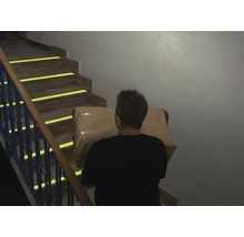 Eine Person trägt ein Paket eine Treppe hinauf, die mit Sicherheitsmarkierungen versehen ist.