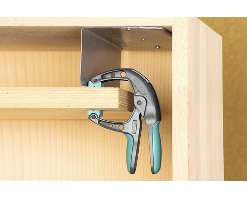 Eine Einhandzwinge fixiert ein Werkstück an einem Möbelstück.