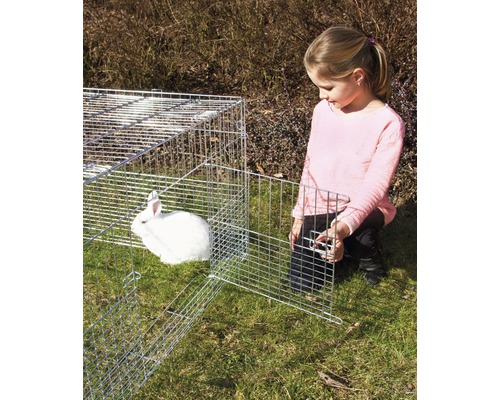 Mädchen öffnet einen Käfig mit einem weißen Kaninchen im Garten