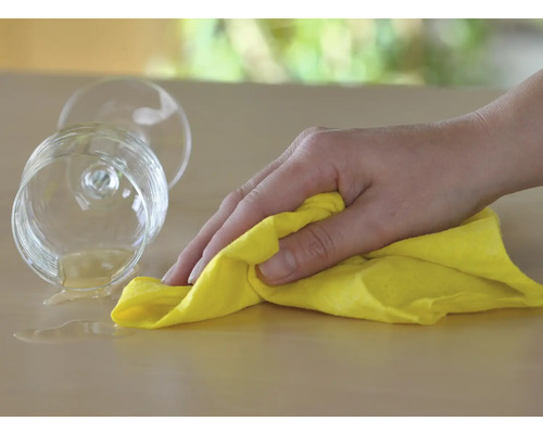 Reinigungskraft: Hand wischt verschüttetes Getränk mit Reinigungstuch auf Tisch.