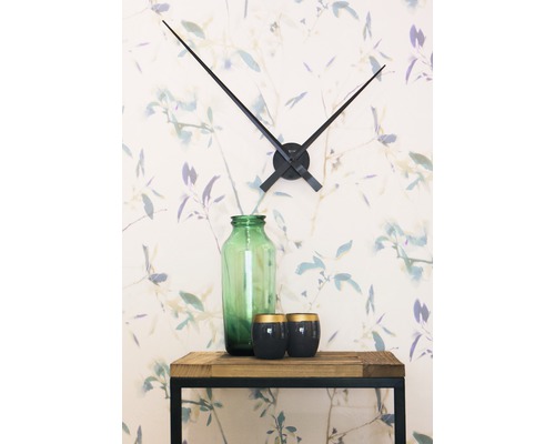 Dekoration mit Wanduhr, Glasvase und Kerzen auf einem Holztisch vor einer floralen Tapete