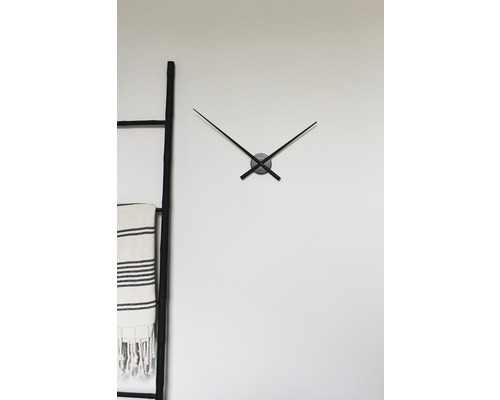 Wanduhr mit Zeigern neben einer Leiter mit Handtuch