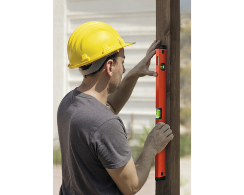 Mann mit Schutzhelm und Wasserwaage an einem Holzpfosten