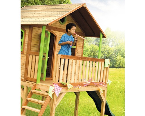 Holzspielhaus mit Rutsche und einem Kind auf der Veranda, das in ein Partyhütchen bläst
