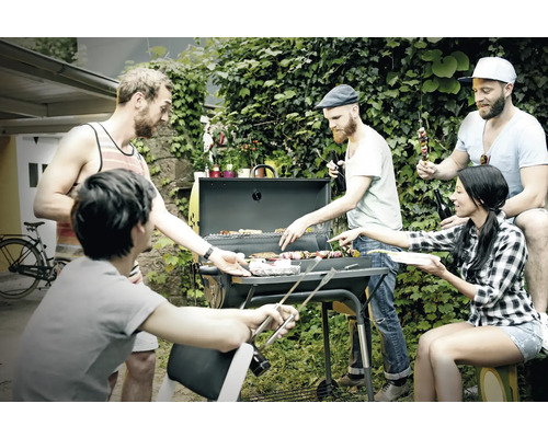 Eine Gruppe von Freunden grillt im Garten mit einem Holzkohlegrill und genießt die Zeit zusammen.