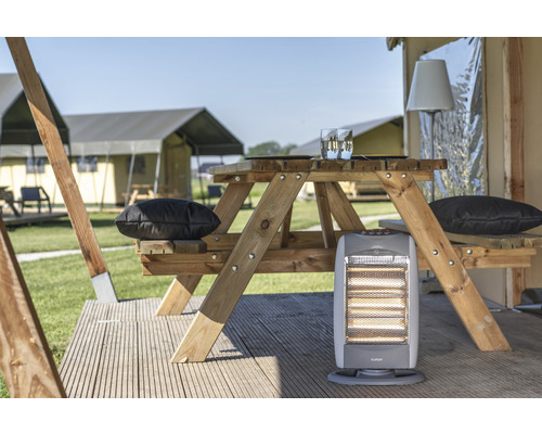 Szene mit einem Holz-Picknicktisch, Kissen und einem Heizgerät vor Zelten