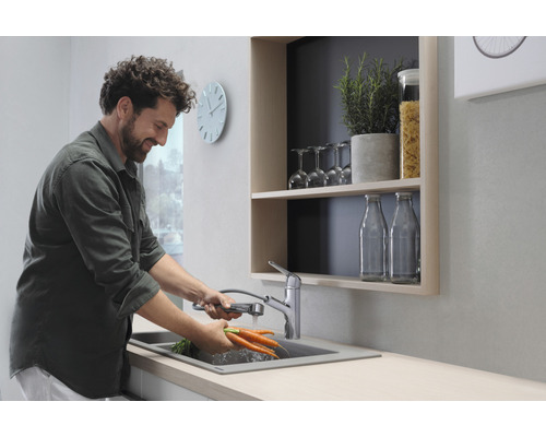 Mann wäscht Karotten in einer Küchenspüle mit ausziehbarer Armatur.