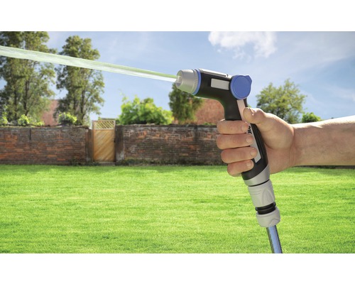 Hand hält Gartenspritze mit Wasserstrahl vor Gartenkulisse