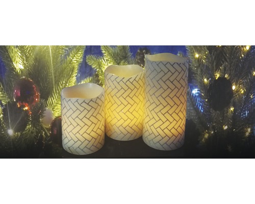 Drei dekorative LED Kerzen mit Ziegelmuster vor einem Weihnachtsbaum
