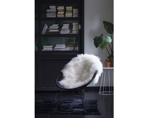 Szene mit schwarzem Sessel, Schaffell, Bücherregal und Pflanze für gemütliches Wohnen