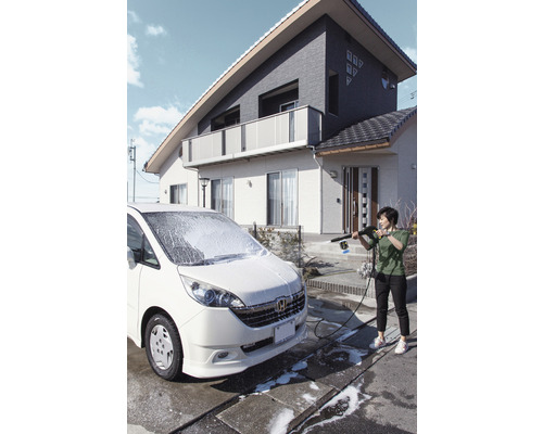 Frau reinigt ein Auto mit einem Hochdruckreiniger vor einem Haus.