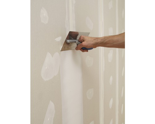 Eine Person glättet Spachtelmasse mit einer Glättkelle auf einer Gipskartonwand.