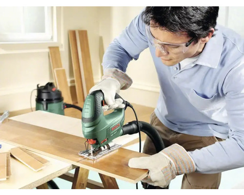 Mann sägt Holzbrett mit Stichsäge, Schutzbrille und Handschuhen