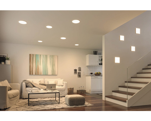 Wohnzimmer mit Deckeneinbaustrahlern und Treppenhaus mit Wandleuchten für eine helle und moderne Atmosphäre