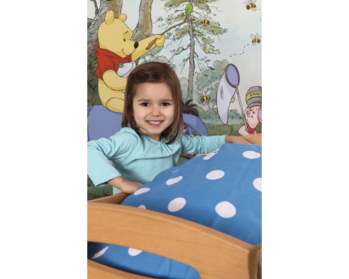 Mädchen im Bett vor einer Wandtapete mit Winnie Puuh Motiv.