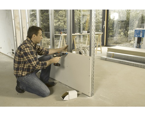 Ein Mann befestigt eine Gipskartonplatte mit einem Akku-Schrauber an einer Metallunterkonstruktion.