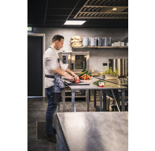 Ein Koch bereitet in einer professionellen Küche Gemüse und Fleisch auf einem Edelstahltisch zu.