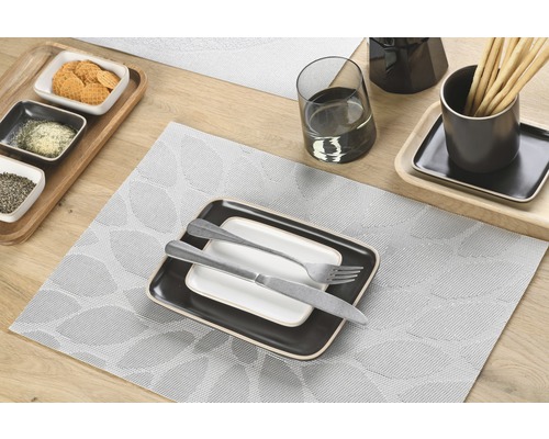 Tischdekoration mit Platzdeckchen, Geschirr und Besteck auf Holztisch