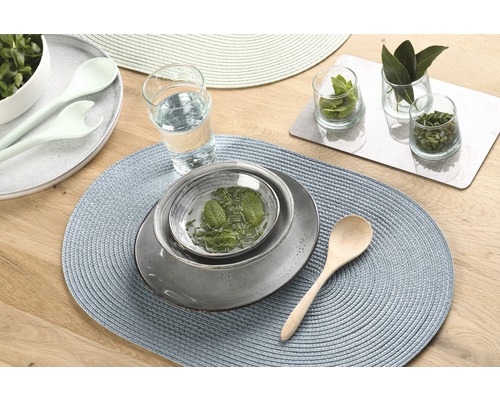 Tischdekoration mit Platzsets, Geschirr, Glas und Kräutern auf einem Holztisch