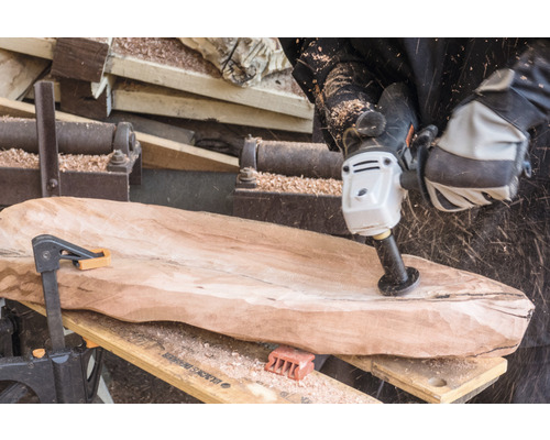 Ein Handwerker bearbeitet ein Holzbrett mit einem Schleifwerkzeug.