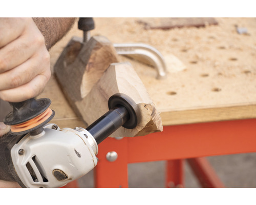 Eine Person benutzt eine Flex mit einem Holzschleiferaufsatz, um ein Stück Holz auf einer Werkbank zu bearbeiten.