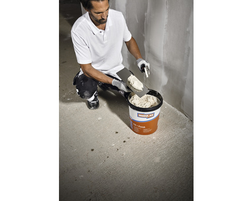 Mann nimmt Spachtelmasse aus einem Eimer. Geeignet zum Verputzen und Spachteln.