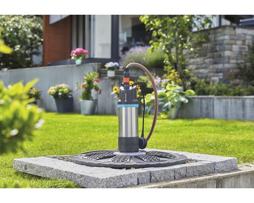 Gartenszene mit einer Gardena Tauchdruckpumpe auf einem Steinplatz, die Wasser ableitet