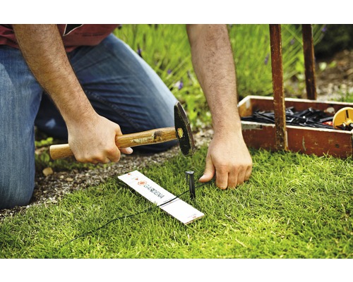 Eine Person hämmert einen Gardena Micro-Drip-System-Rohrhalter in den Rasen