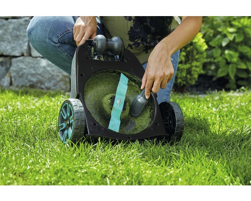 Eine Person reinigt einen Rasenmäher auf einer Rasenfläche.