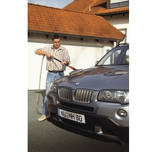 Mann wäscht ein Auto mit einer Waschbürste und einem Wasserschlauch