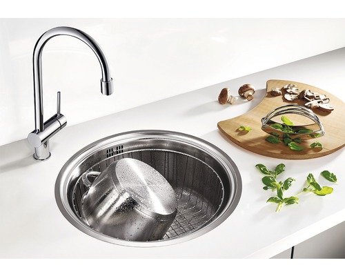 Küchenszene mit rundem Spülbecken, Armatur, Schneidebrett, Topf und Zutaten.