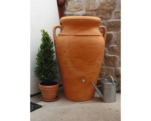 Terrakottafarbene Wasserspeicher Amphore mit Wasserhahn, daneben eine Gießkanne und ein Topf mit Buchsbaum