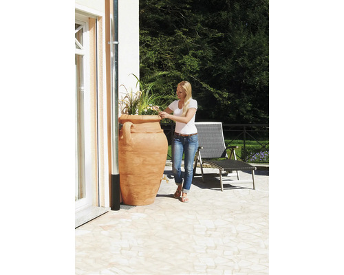 Frau gießt Pflanzen in einem Terrakotta Pflanzgefäß auf einer Terrasse.