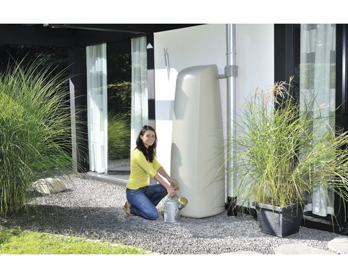 Frau befüllt eine Gießkanne an einem stehenden Wassertank im Garten.