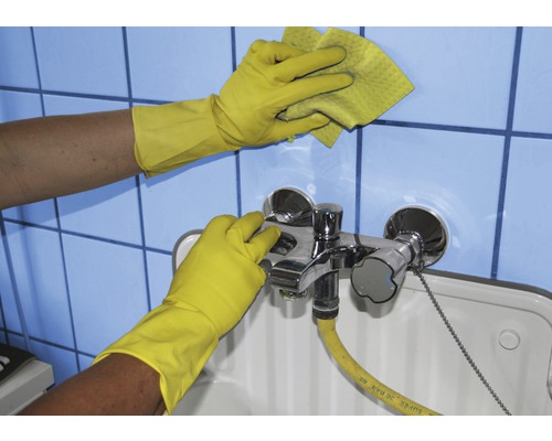 Reinigungskraft mit Gummihandschuhen reinigt Waschbecken und Fliesen mit einem Schwamm