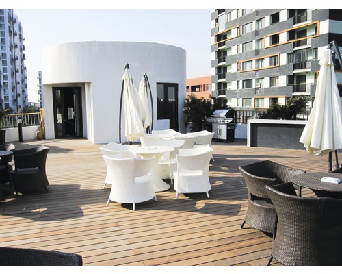 Terrasse mit Gartenmöbeln aus Rattan und Sonnenschirmen vor einem Gebäude