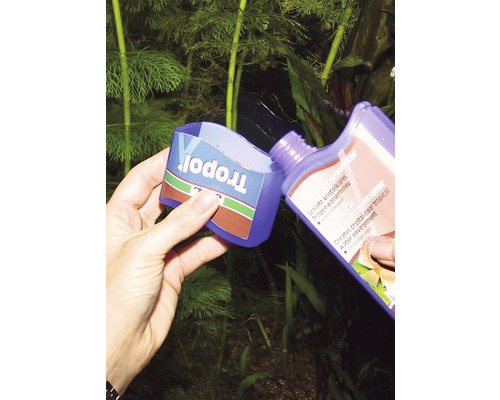 Eine Person gießt Tropopol Wasseraufbereiter in einen Messbecher vor einer Aquariumpflanze.