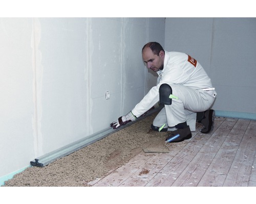 Handwerker nivelliert Trockenschüttung mit einer Richtlatte auf einem Holzboden.