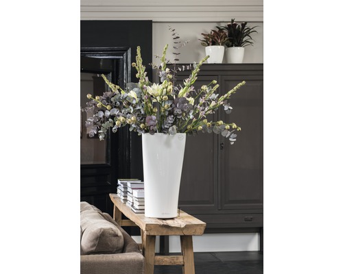 Hohe, weiße Blumenvase mit Blumenstrauß auf einer Holzbank in einem Zimmer