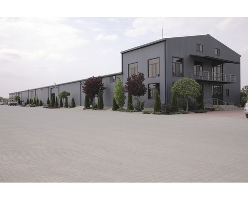 Außenansicht eines großen Industriegebäudes mit Parkplatz und Bäumen