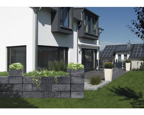 Graue Gartenmauer aus Betonsteinen mit Bepflanzung vor einem Wohnhaus.