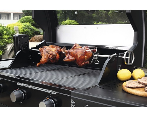 Gasgrill mit zwei Brathähnchen auf einem Drehspieß und Zitronen auf einer Holzplatte