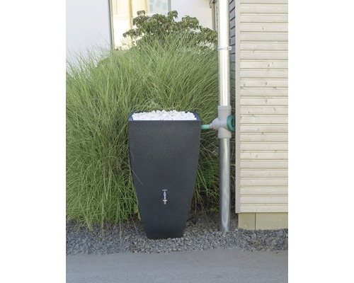 Regenspeicher mit Füllmaterial neben einem Fallrohr an einem Haus