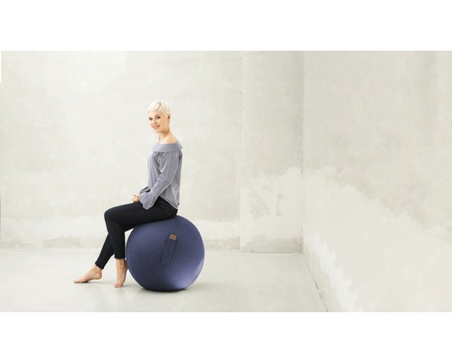 Frau sitzt auf einem blauen Gymnastikball in einem hellen Raum.