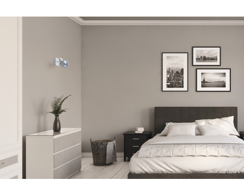 Schlafzimmer mit Bett, Kommode, Nachttisch, Wandleuchte und gerahmten Bildern