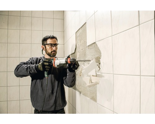 Mann entfernt Fliesen mit einem Bohrhammer