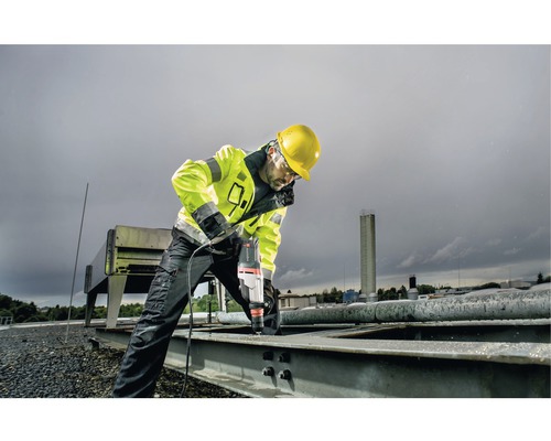 Ein Bauarbeiter bohrt mit einer Bohrmaschine ein Loch in ein Metallteil auf einem Dach.