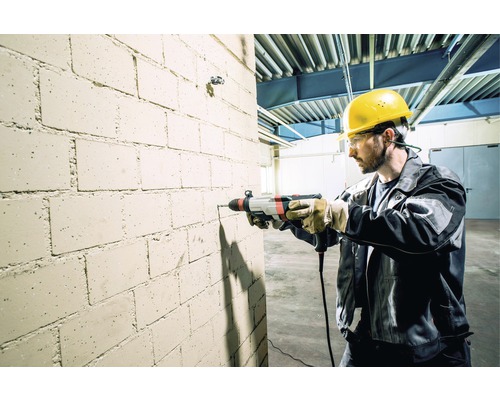 Ein Mann bohrt mit einem Bohrhammer in eine Ziegelwand.
