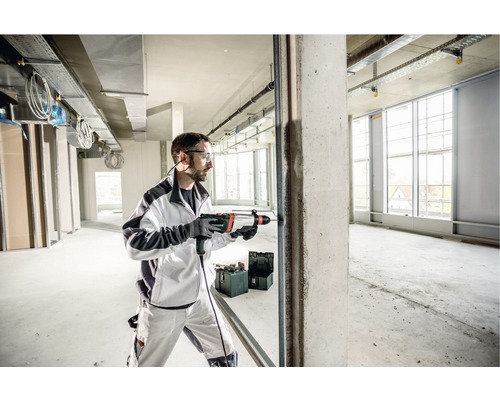 Ein Mann bohrt mit einer Schlagbohrmaschine ein Loch in eine Betonwand in einem Rohbau