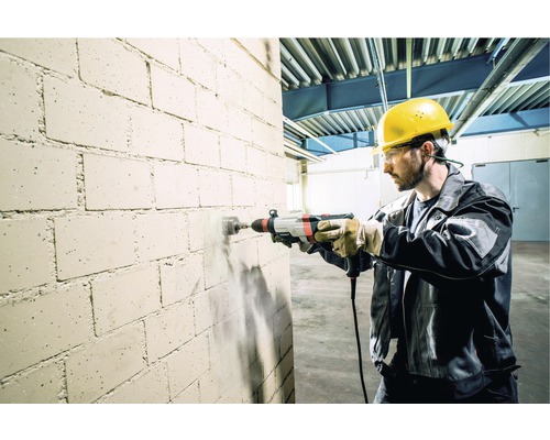 Ein Mann bohrt mit einer Schlagbohrmaschine ein Loch in eine Ziegelsteinmauer.
